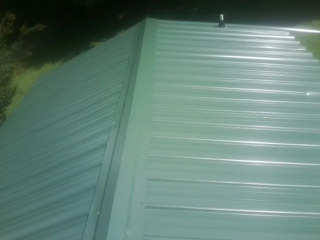 New green metal panels meeting at the ridge of a roof — Flat Roof Repair work by our crew in Clio